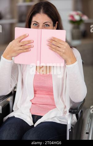 Glückliche behinderte Frau sitzt im Rollstuhl und liest Stockfoto