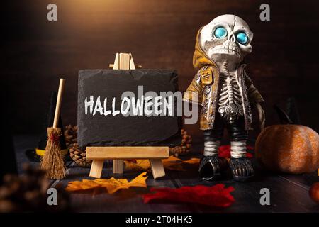 4. Oktober 2023: Herbst- und Halloween-Dekoration um eine Tafel mit Inschrift: Halloween. Skelett mit Hexenbesen gruselige KONZEPTFOTOMONTAGE *** Herbst und Halloween Dekoration um eine Kreidetafel mit Aufschrift: Halloween. Skelett mit Hexenbesen Grusel Konzept FOTOMONTAGE Stockfoto