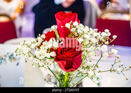 Rote Rosen in einem Blumenstrauß in einem Etui bilden ein dekoratives Herzstück auf einem Tisch auf einer Party Stockfoto