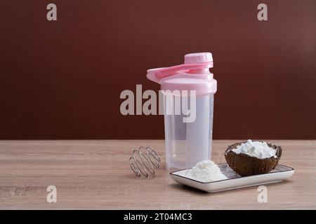 Eine Handvoll weißes Pulver und eine Mixflasche zum Mischen von Zutaten für die Sporternährung stehen auf einem Tisch. Eine Person bereitet einen Kokosprotein-Shake vor. A uns Stockfoto