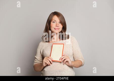 Süße junge, lächelnde schwangere Frau, die ein Buch mit leerem Titelmockup hält, Außenporträt Stockfoto