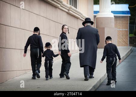 Ein Vater und seine 4 identisch gekleideten Söhne steigen einen Hang hinauf, um eine Synagogenfeier zu besuchen. In Kiryas Joel, Orange County, New York. Stockfoto