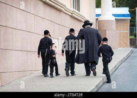 Ein Vater und seine 4 identisch gekleideten Söhne steigen einen Hang hinauf, um eine Synagogenfeier zu besuchen. In Kiryas Joel, Orange County, New York. Stockfoto