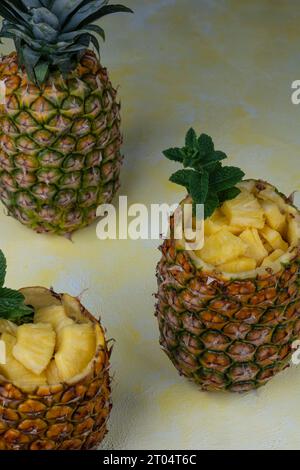 Frische und saftige Ananasstücke serviert in zwei ausgehöhlten Ananasfrüchten, im Hintergrund eine ganze Ananasfrucht Stockfoto