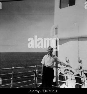 Ein Passagier, der neben einer britischen Rettungsboje steht. Dieses Foto stammt von einem nicht zugeschriebenen persönlichen Fotoalbum einer Kreuzfahrt nach New York vom 29. Juni bis 13. August 1956. Segeln von Liverpool an Bord des Cunard-Schiffes M.V. Britannic und Rückfahrt von New York nach Southampton an Bord des Cunard-Schiffes R.M.S. Queen Mary. Die durchschnittliche Größe der Originalfotos betrug 4 x 3 Zoll. Stockfoto