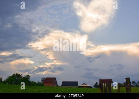 Landhäuser und eine grüne Wiese. Die Sonne hinter den Wolken erleuchtet sowohl den Himmel als auch die Wolken mit romantischem Licht Stockfoto