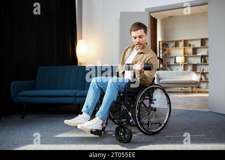 Körperliche Rehabilitation für Behinderte. Glücklicher Kerl im Rollstuhl, der zu Hause Übungen mit Kurzhantel macht. Fröhlicher, behinderter junger Mann, der trainiert Stockfoto