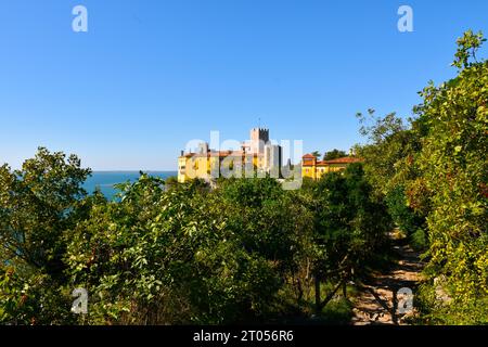 Der Weg führt durch einen mediterranen Wald und die Burg Duino dahinter in Duino-Aurisina, Italien Stockfoto