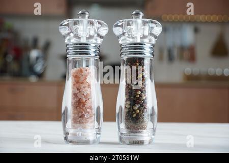 Salz- und Pfeffermühle. Getrocknete ganze Samen von schwarzem Pfeffer und rosa Himalaya-Salz Stockfoto