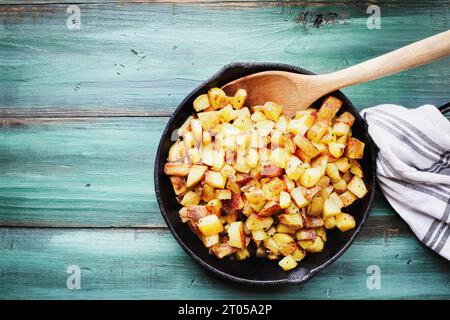 Blick von der Tischplatte auf eine gusseiserne Pfanne gefüllt mit frischen knusprigen goldenen Yukon-Gold frittierten Kartoffeln. Flach. Gemeinkosten. Stockfoto