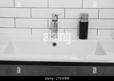 Modernes Waschbecken. Stilvolles weißes Waschbecken mit Wasserhähnen in moderner Einrichtung. Wasserhahn aus Chrommaterial. Haushaltsgeräte. Graues Badezimmer. Haushaltsgeräte Stockfoto