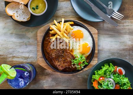 Vietnamesisches Rindersteak mit Pommes frites, Spiegeleiern, Baguette, serviert mit Limonadengetränk und Gemüsesalat Stockfoto