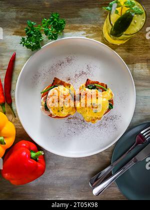 Englischer Muffin mit pochierten Eiern, Speck und Hollandaise-Sauce mit Gemüse Stockfoto