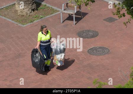 Eine Frau im Reinigungssektor trägt Müllsäcke, die sie in die Mülltonnen werfen. Barcelona, Katalonien, Spanien. Stockfoto