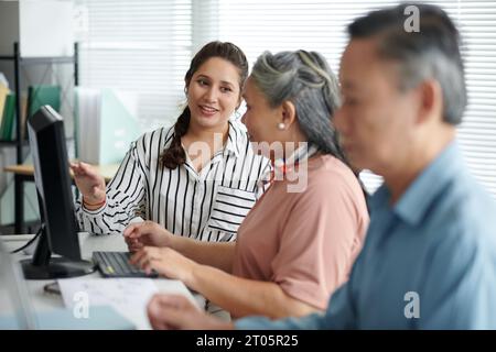 Junge Frau, die Senioren hilft, grundlegende Computerfähigkeiten zu erlernen Stockfoto