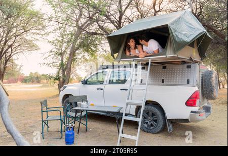 Junges Paar, das in einem Zelt auf dem Dach eines Geländewagens in einem Wüstencamp liegt Stockfoto