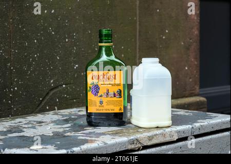 Eine geöffnete Flasche Buckfast Tonic Wine, die auf einer Stadtstraße neben einem Milchkarton in Glasgow, Schottland, Großbritannien, Europa entsorgt wurde Stockfoto