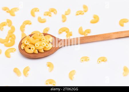 Ungekochte Chifferi Rigati Pasta in Holzlöffel auf weißem Hintergrund. Fett und ungesunde Lebensmittel. Verstreute Klassische Trockene Makkaroni. Italienische Kultur und Küche. Rohe Pasta Stockfoto
