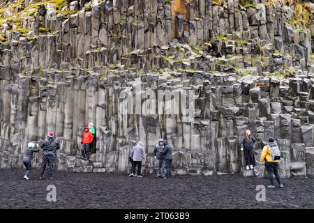 Island Touristen am schwarzen Sandstrand Vik, oder Reynisfjara Beach, Island South Coast Tour, Basaltklippen und Ergebnisse vulkanischer Aktivität; Vik, Island Stockfoto