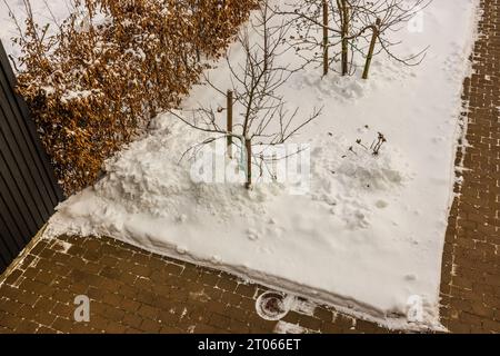 Blick von oben auf den Garten mit Pflastersteinpflasterweg, der von Schnee befreit ist, im schneebedeckten Innenhof vor dem Haus. Schweden. Stockfoto