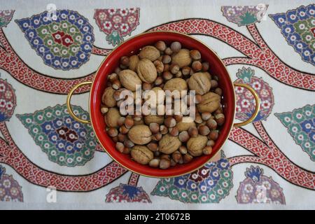 Walnüsse und Haselnüsse stehen in großer roter Schüssel. Haselnüsse und Walnüsse stehen in einer roten Schüssel. Haselnüsse und Walnüsse auf dem Tisch. Stockfoto