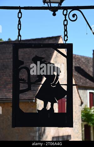 Ein Metallschild zeigt einen mittelalterlichen Bäcker, der seinen Brotbackofen in Urval, Dordogne, Frankreich, pflegt. Das Dorf hat einen Gemeinschaftsofen aus dem 15. Jahrhundert. Stockfoto