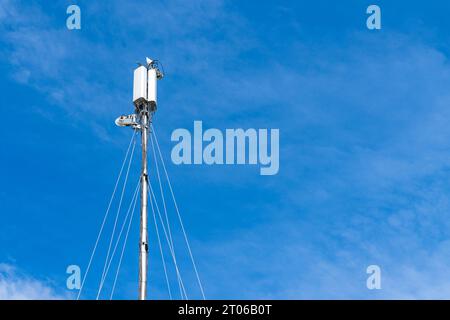 Die Spitze eines Sendemastes für die mobile Kommunikation vor einem Hintergrund des blauen Himmels mit hellen Wolken. Stockfoto