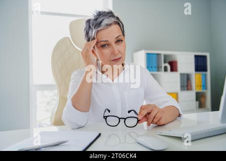 Foto von müder depressiver Angestellter tragen weißes Hemd mit Kopfschmerzen am Arbeitsplatz Stockfoto