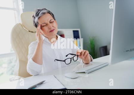 Foto von überarbeiteter müder Dame Angestellte tragen weißes Hemd, das moderne Gadget arbeitet und Kopfschmerzen am Arbeitsplatz hat Stockfoto