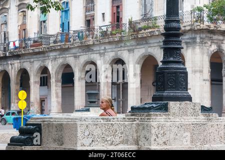 Eine Frau sitzt auf den Steinbänken des Paseo del Prado im Stadtzentrum der kubanischen Hauptstadt. Verwitterte Fassade von Gebäuden im Hintergrund Stockfoto