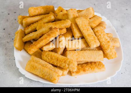 Knusprige panierte Fischstäbchen aus wild gefangenem Alaska Pollock Nahaufnahme auf weißer Platte auf hellgrauem Steinhintergrund Stockfoto