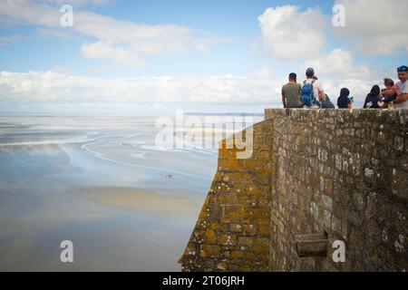 MONT SAINT MICHEL, AUGUST 2023 - Touristen bewundern an einem Sommertag die Aussicht auf die Bucht bei Ebbe von den Mauern der Abtei Mont Saint Michel. Stockfoto