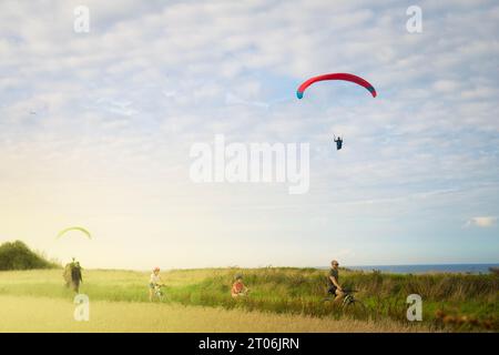 VIERVILLE SUR MER, AUGUST 2023 - der Gleitschirmflugplatz am Strand von Omaha, mit Menschen auf Fahrrädern bei Sonnenuntergang. Stockfoto