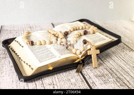 Rosenkranzperlen und Kruzifix Kreuz auf heiliger Bibel mit Kerzen in der Kirche. Stockfoto