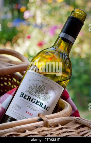 Bergerac Weißweinflaschenetikett 2022 im Picknickkorb im sonnigen Garten mit Blumenmuster im Freien. Südwestfrankreich trockener Weißwein. Semillon/Sauvignon Blanc Stockfoto