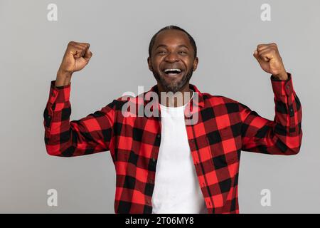 Ein sehr glücklicher, schwarz bärtiger Mann, der ein rotes kariertes Hemd trägt, geballte Fäuste, die den Sieg feiern Stockfoto