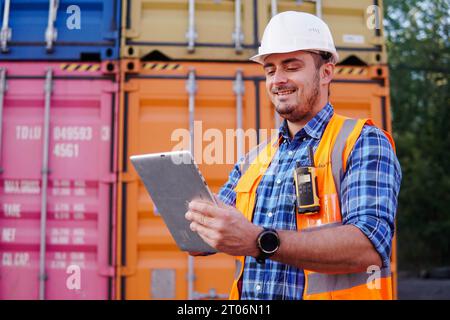 Container-Lagerarbeiter in Uniform verwendet ein digitales Tablet, um den Bestand in einem großen Containerhof zu inspizieren. Logistik und Export von Unternehmen. Stockfoto