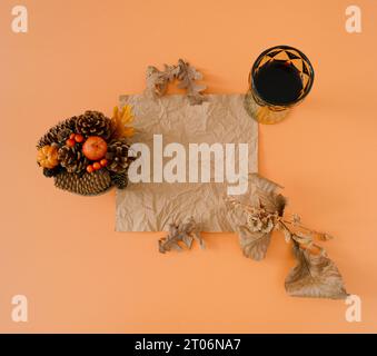 Kreatives Herbst- oder Herbstlayout mit Blättern, kleinen Kürbissen und Glas Rotwein auf pastellorangen Hintergrund mit zerknitterter Papierkarte. Stockfoto
