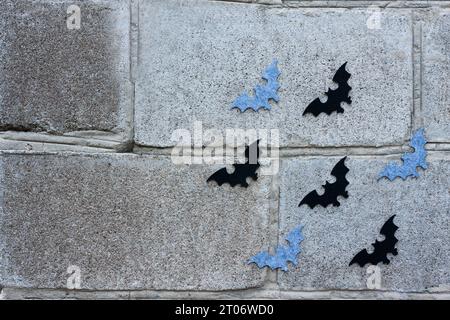 Halloween-Hintergrund. Festliche Einrichtung: Schwarze und graue Filzfledermäuse fliegen auf einer Steinmauer. Kopierbereich Stockfoto