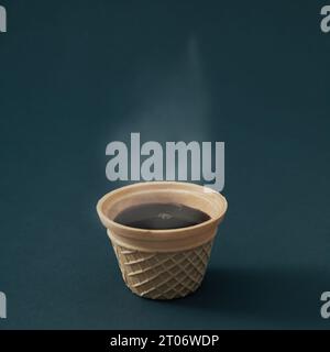 Nahaufnahme von heißem dampfendem Kaffee in Waffeleiskegel vor schwarzem Hintergrund. Minimales Kaffeeästhetisches Konzept. Creative Ice Coffee ide Stockfoto