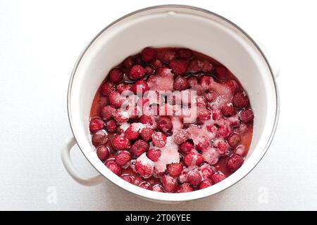 Die Phase der Herstellung von hausgemachter Erdbeermarmelade. Reife Beeren werden in einem Topf mit Zucker bestreut. Sommerzeit für die Konservierung von Beerenmarmelade. Draufsicht Stockfoto