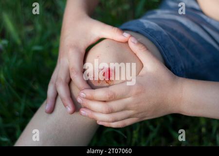 Nahaufnahme einer frischen, sturzbedingten Blutung am Knie des Kindes. Kindheitstrauma, Schmerz, Unachtsamkeit, Unfall. Sommer, Outdoor Stockfoto