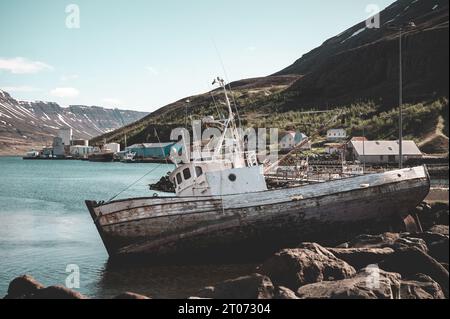 Altes Schiffswrack im Hafen von Seydisfjordur, Island, Gebirge und Meer im Hintergrund Stockfoto