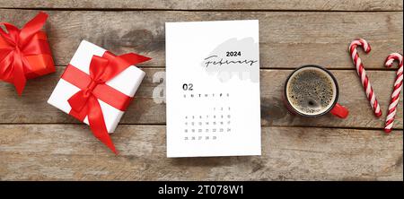 Papierkalender für Februar 2024 mit Geschenkboxen, Zuckerstangen und einer Tasse Kaffee auf hölzernem Hintergrund Stockfoto