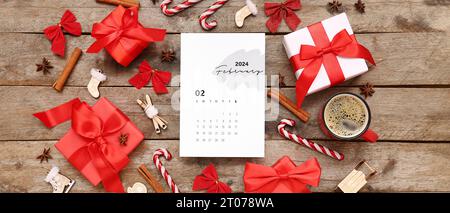 Papierkalender für Februar 2024 mit Geschenkboxen, Weihnachtsdekorationen und Tasse Kaffee auf hölzernem Hintergrund Stockfoto