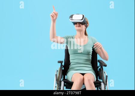 Junge Frau im Rollstuhl mit VR-Brille auf blauem Hintergrund Stockfoto