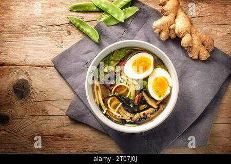 Miso-Suppe mit Nudeln, Nori-Algen, Schneeroben, Ingwer und einem Ei in einer Schüssel auf einem rustikalen Holztisch, Draufsicht von oben, Kopierraum, ausgewählter Fokus Stockfoto