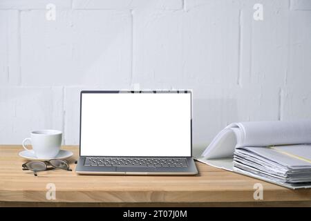 Modell eines Laptops mit leerem weißen Bildschirm, Aktenordner und Kaffeetasse auf einem Holztisch vor einer weiß lackierten Wand, Konzept für Büro und Büro Stockfoto
