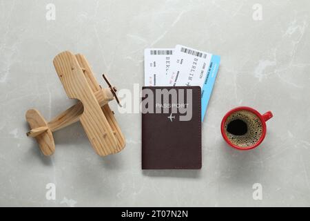 Flache Lay-Komposition mit Reisepass, Tickets, Tasse Kaffee und Holzflugzeug auf hellem Marmortisch. Geschäftsreise Stockfoto