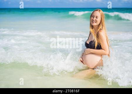 Strahlende schwangere Frau im Badeanzug, inmitten der atemberaubenden Kulisse eines türkisfarbenen Meeres. Ruhige Schönheit der Mutterschaft am Ufer Stockfoto